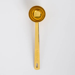 Gold measuring spoon with 'VHYNE' branding on a white background