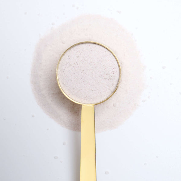 Gold spoon with VitarResiliance powder on a textured white surface