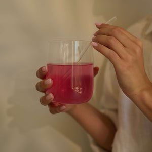 Person holding a glass of mixed berry VitaResilience with a straw against a neutral background