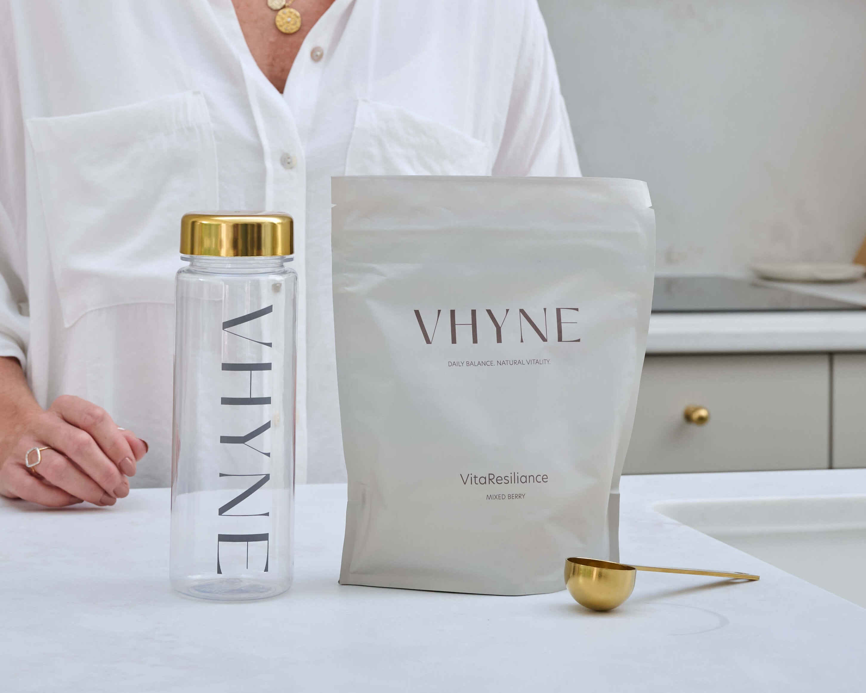 Vhyne branded water bottle, pouch of VitaResiliance powder, and scoop on a kitchen counter
